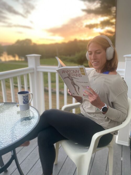 Woman sitting on porch listening to audiobook and reading anatomy trains 4th edition